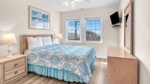 A bedroom with a bed, nightstands, a ceiling fan, a TV, a window, and a painting on the wall.