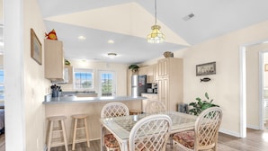 A modern kitchen with a central island, bar stools, and a dining table with wicker chairs.