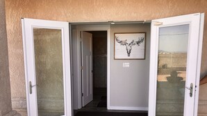 Entrada de hotel com porta de vidro, uma obra de arte emoldurada na parede e chão de concreto.