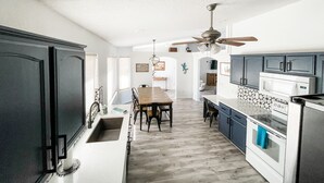 Uma cozinha com área de refeições, armários brancos, mesa de madeira e um ventilador de teto.