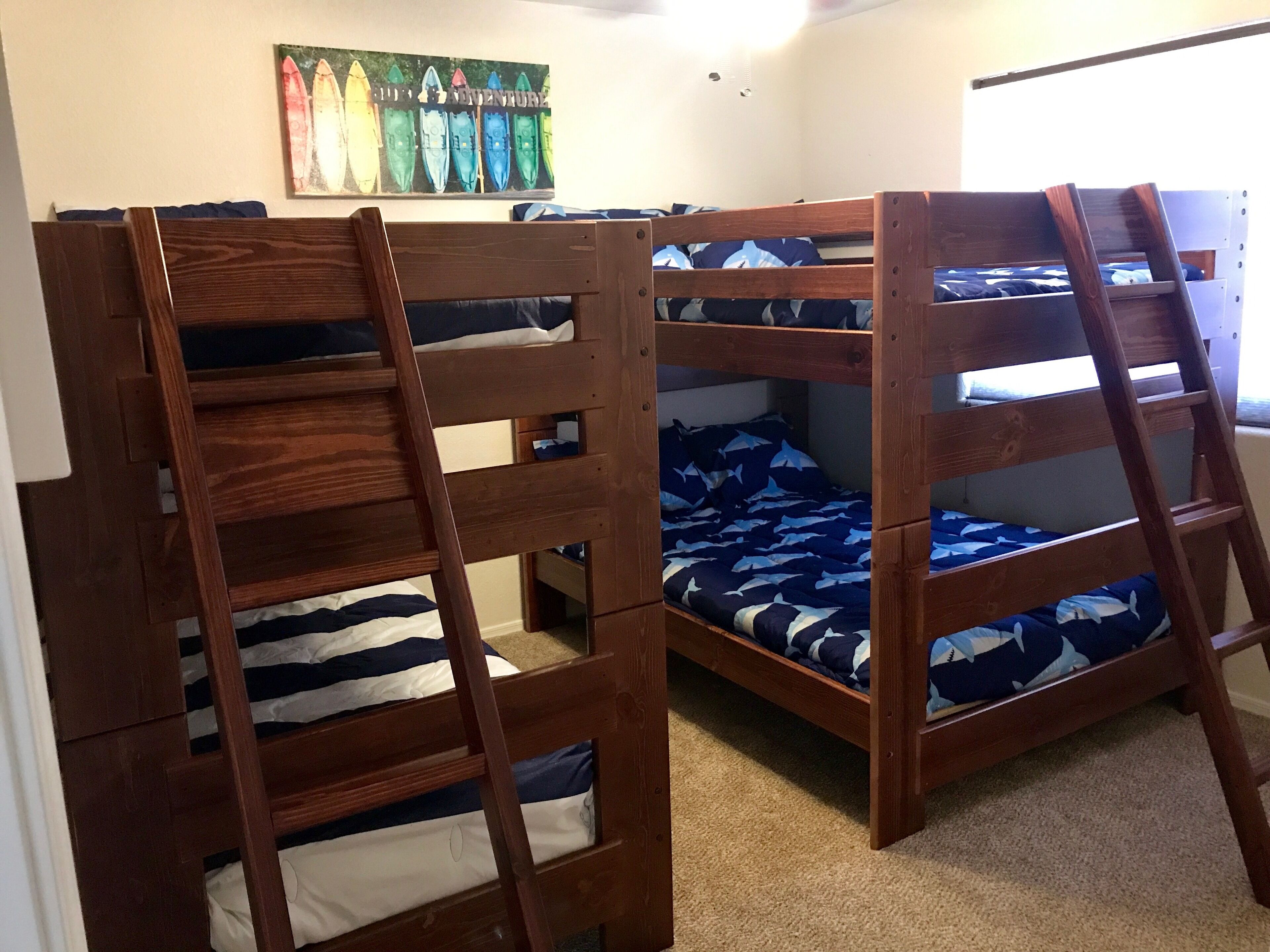 Two bunk beds with a ladder, a wall with a surfboard poster, and a window with blinds.