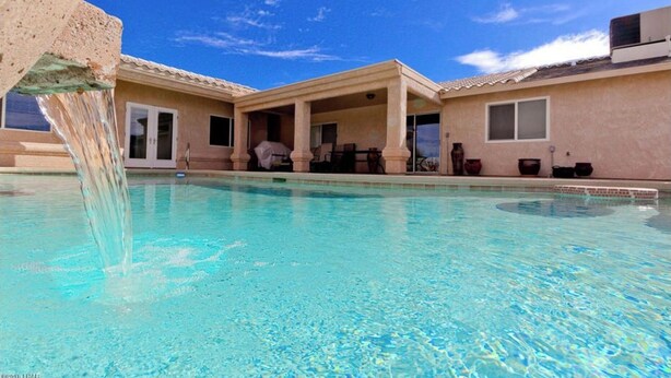 Uma piscina com um recurso aquático, um espaço de varanda coberto e um edifício com telhado ladrilhado.