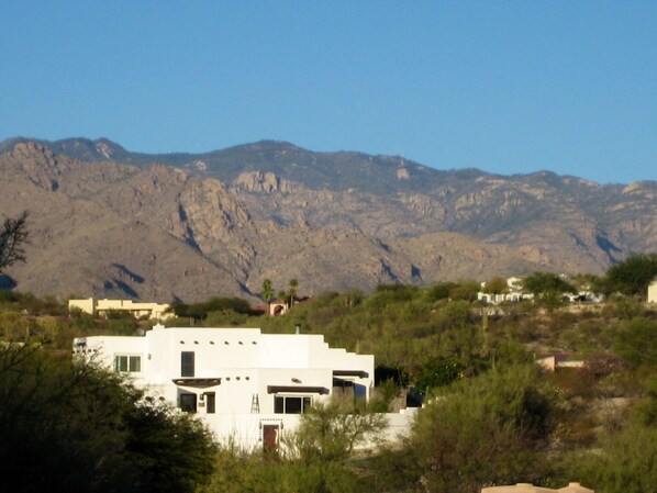 A white building with a flat roof, surrounded by greenery and mountains in the background.