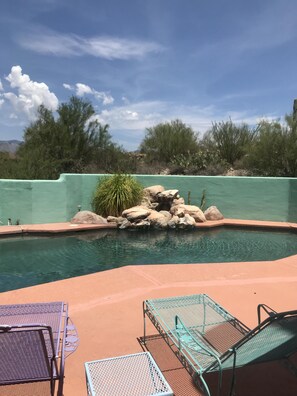 A swimming pool with a rocky edge, surrounded by desert vegetation and a clear sky.