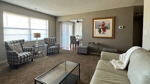 A living room with a beige sofa, two plaid armchairs, a glass coffee table, and a dining area in the background. - Heritage Suites 44 (Manhattan)