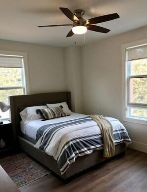 Une chambre à coucher avec un lit, un ventilateur de plafond et deux fenêtres.