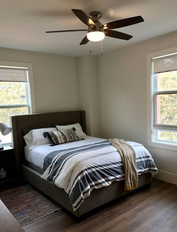 Un dormitorio con una cama, ventilador de techo y dos ventanas.