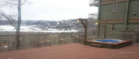 A wooden deck with a hot tub and a small pool, overlooking a snowy landscape with mountains in the distance.