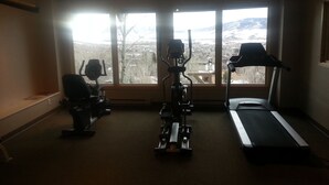 Ein Fitnessraum mit Cardiogeräten und Laufband, große Fenster mit Blick auf die Stadt.