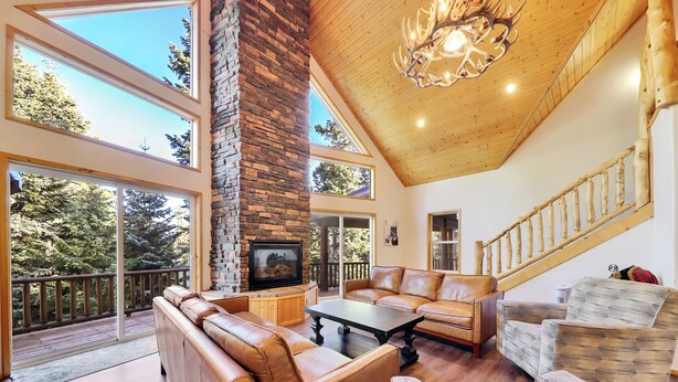 A spacious living area with a stone fireplace, leather sofas, and a wooden staircase. - Empty Saddle - 6 bedrooms / 3.5 baths (Duck Creek Village)