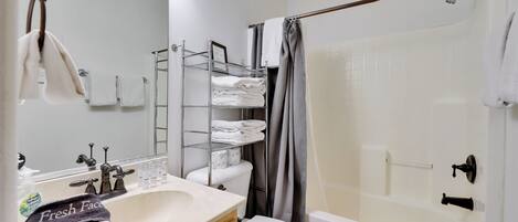 A bathroom with a white sink, a toilet, a shower with a glass door, and a towel rack with neatly folded towels.
