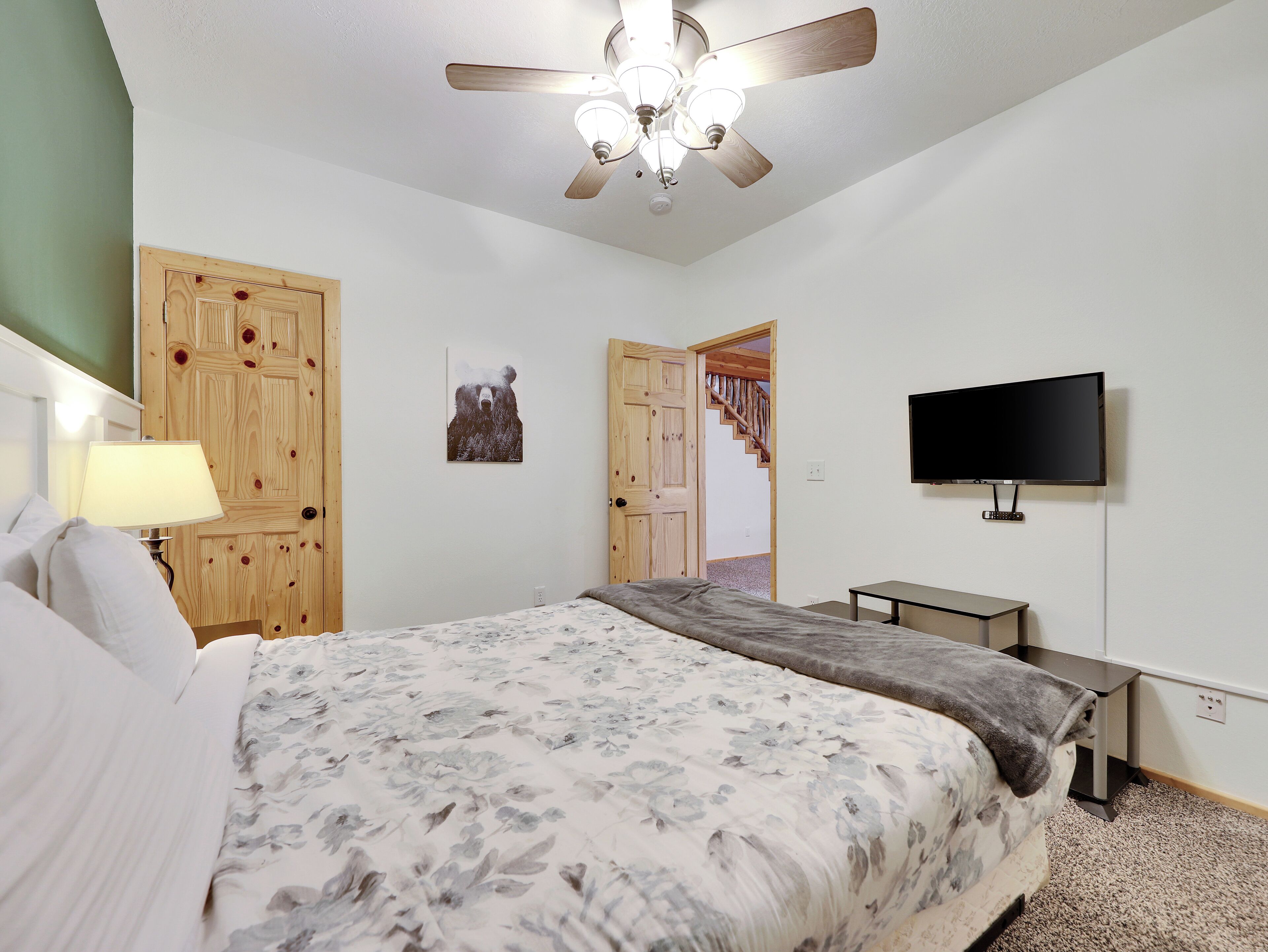 A bedroom with a bed, a desk, a TV, and a ceiling fan.