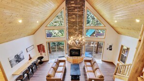 A spacious loft-style living area with a fireplace, wooden ceiling, and large windows offering views of the outdoors. - Empty Saddle - 6 bedrooms / 3.5 baths (Duck Creek Village)