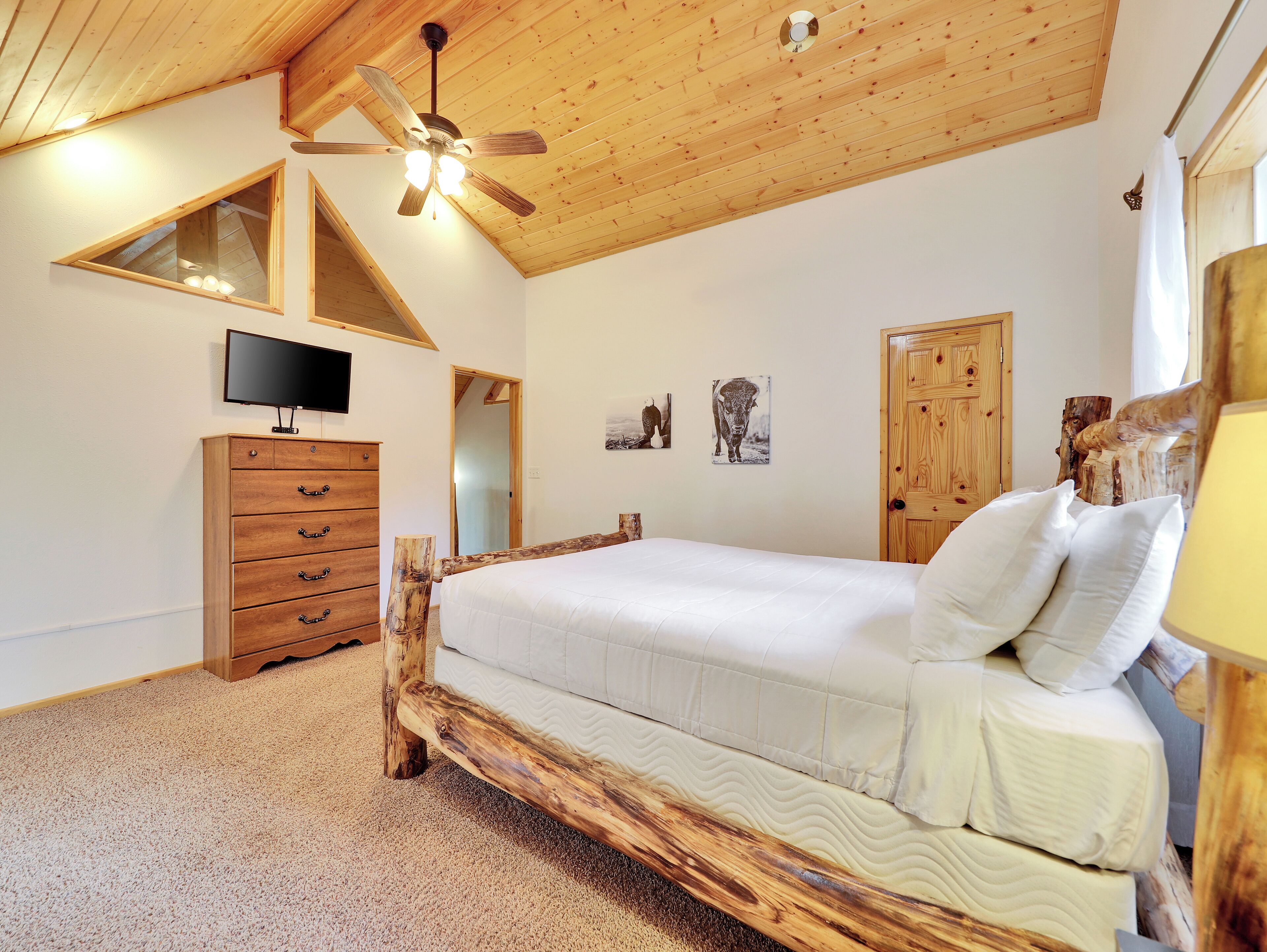 A bedroom with a wooden bed frame, a television on the wall, and a ceiling fan.