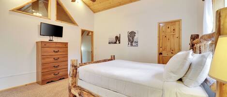 A bedroom with a wooden bed frame, a television on the wall, and a ceiling fan.