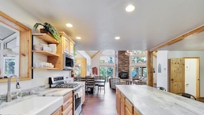 A spacious kitchen with wooden cabinets, a large island, and a stone fireplace. - Empty Saddle - 6 bedrooms / 3.5 baths (Duck Creek Village)