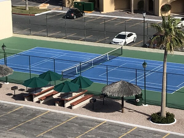 A tennis court with seating and umbrellas, surrounded by a parking area and palm trees. - Remodeled Luxury Condo w/Breathtaking View Of The Sea of Cortez on Sandy Beach (Puerto Penasco)