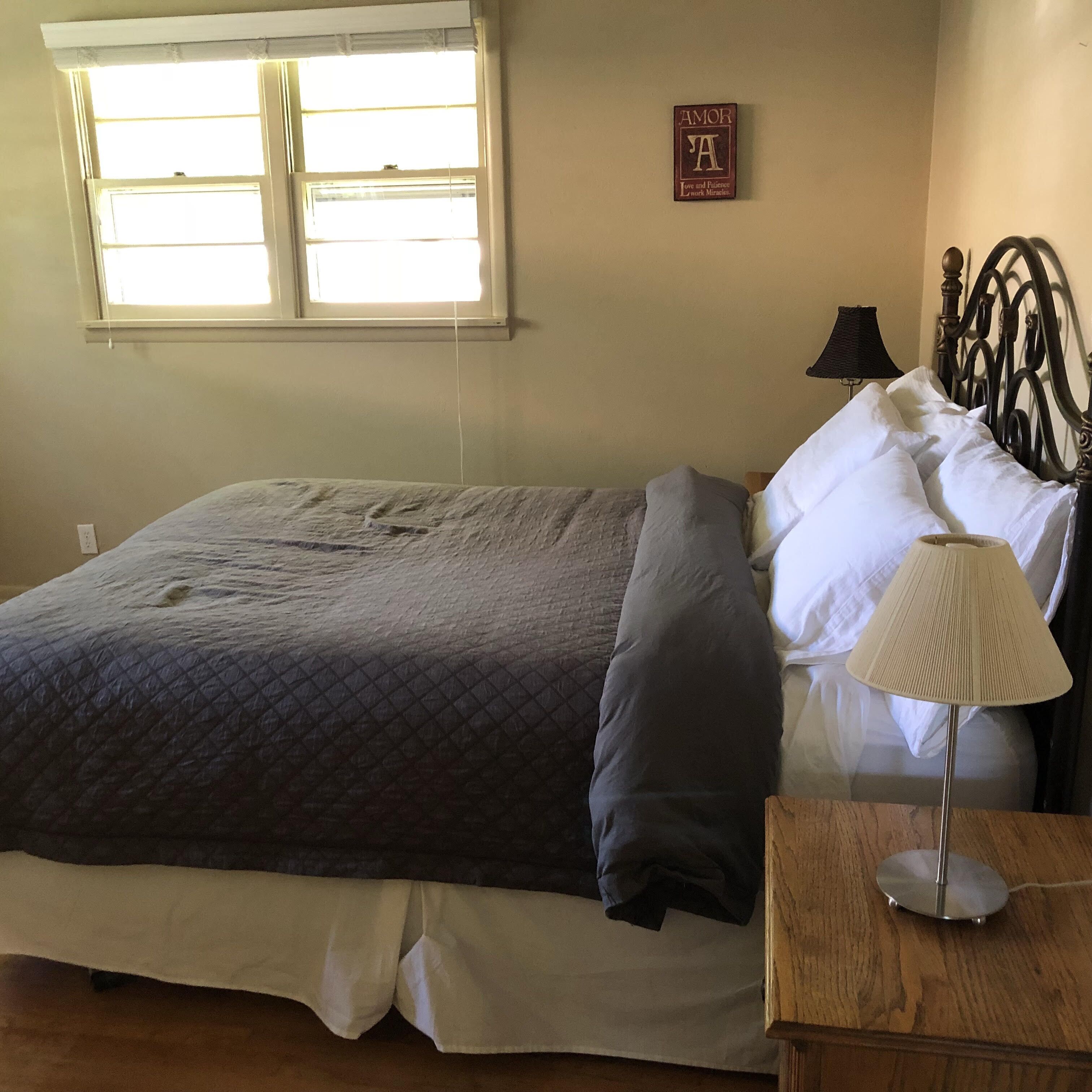 Ein Schlafzimmer mit Bett, Kissen, einer Nachttischlampe, einem Fenster und einer Wanddekoration.