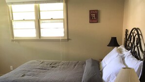 A bedroom with a bed, pillows, a bedside lamp, a window, and a wall decoration. - PETS welcome! CSU/mid-town Home!  (Fort Collins)
