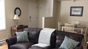 A living room with a brown leather sofa, patterned throw pillows, a white throw blanket, a wooden coffee table, a wall clock, a framed picture, and a dining area with a white table and chairs. - PETS welcome! CSU/mid-town Home!  (Fort Collins)