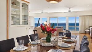 A dining area with a view of the ocean, a dining table set with plates and glasses, and a cabinet with glass doors.