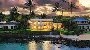 A beachfront property with a large house featuring multiple rooms, a pool, and a well-maintained garden.