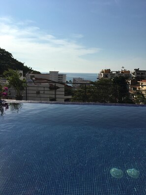 An infinity pool with a clear view of the sea and buildings in the background. - Modern Condo in Bella Loma, steps from the beach, with Ocean views! (Puerto Vallarta)