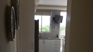 Ett modernt kök med vita skåp, ett stort fönster och en platt-TV som är monterad ovanför bänkskivan.