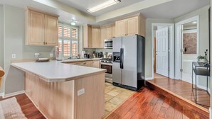 A modern kitchen with wooden cabinets, a central island, stainless steel appliances, and a wooden floor. - Ski-In/Ski-Out, Hot Tub, Walk to Main Street (Park City)