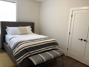 A bedroom with a bed, pillows, a striped bedspread, a bench, and a white door.