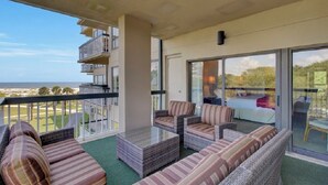 A balcony with wicker furniture, a glass door leading outside, and a view of the beach.