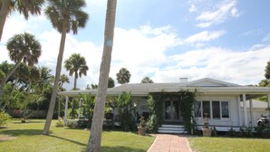 A single-story house with a covered porch, surrounded by a well-maintained lawn and palm trees. - Old Florida Charm, House on the Indian River Lagoon with 250 ft Dock New Listing (Fort Pierce)
