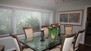 A dining room with a glass-top table surrounded by four upholstered chairs with a diamond pattern. A vase with red and white flowers is placed on the table. - Old Florida Charm, House on the Indian River Lagoon with 250 ft Dock New Listing (Fort Pierce)