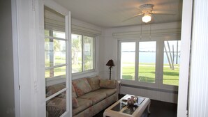 A room with a white ceiling fan, a floral sofa, a glass coffee table, and large windows offering a view of a grassy area and water. - Old Florida Charm, House on the Indian River Lagoon with 250 ft Dock New Listing (Fort Pierce)