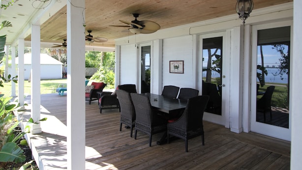 A covered outdoor patio with a wooden deck, a table with chairs, ceiling fans, and large windows with a view of the outdoors. - Old Florida Charm, House on the Indian River Lagoon with 250 ft Dock New Listing (Fort Pierce)