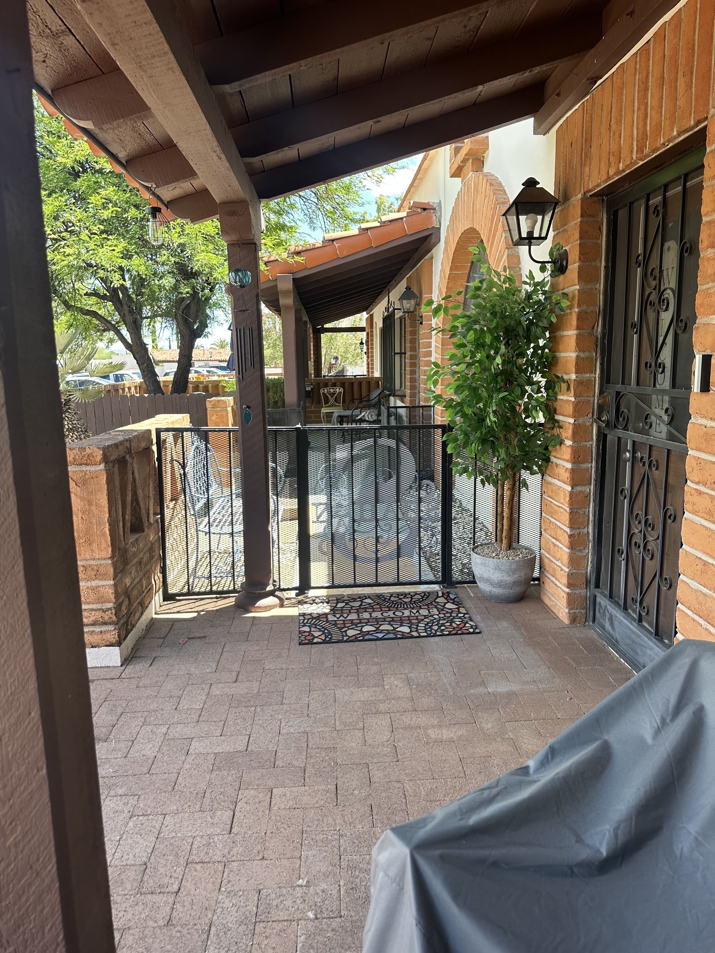 A covered patio with a wrought iron gate, a potted plant, and a welcome mat.