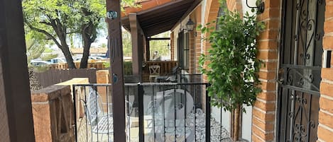 A covered patio with a wrought iron gate, a potted plant, and a welcome mat.