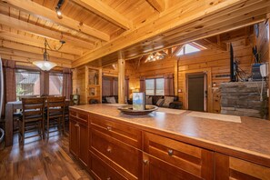 A wooden cabin interior with a kitchen area, dining table, and chairs.