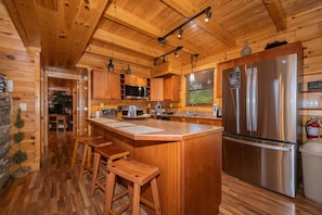 L’intérieur d’un chalet en bois comprend une cuisine, des tabourets de bar en bois, un grand réfrigérateur et un mur en pierre.