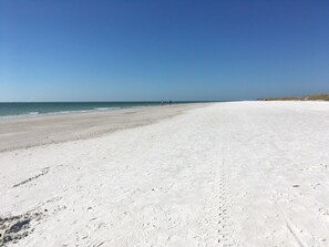 Uma extensa praia de areia com céu azul e límpido.