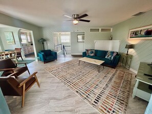 Uma sala de estar com ventilador de teto, sofá, mesa de centro e tapete estampado.