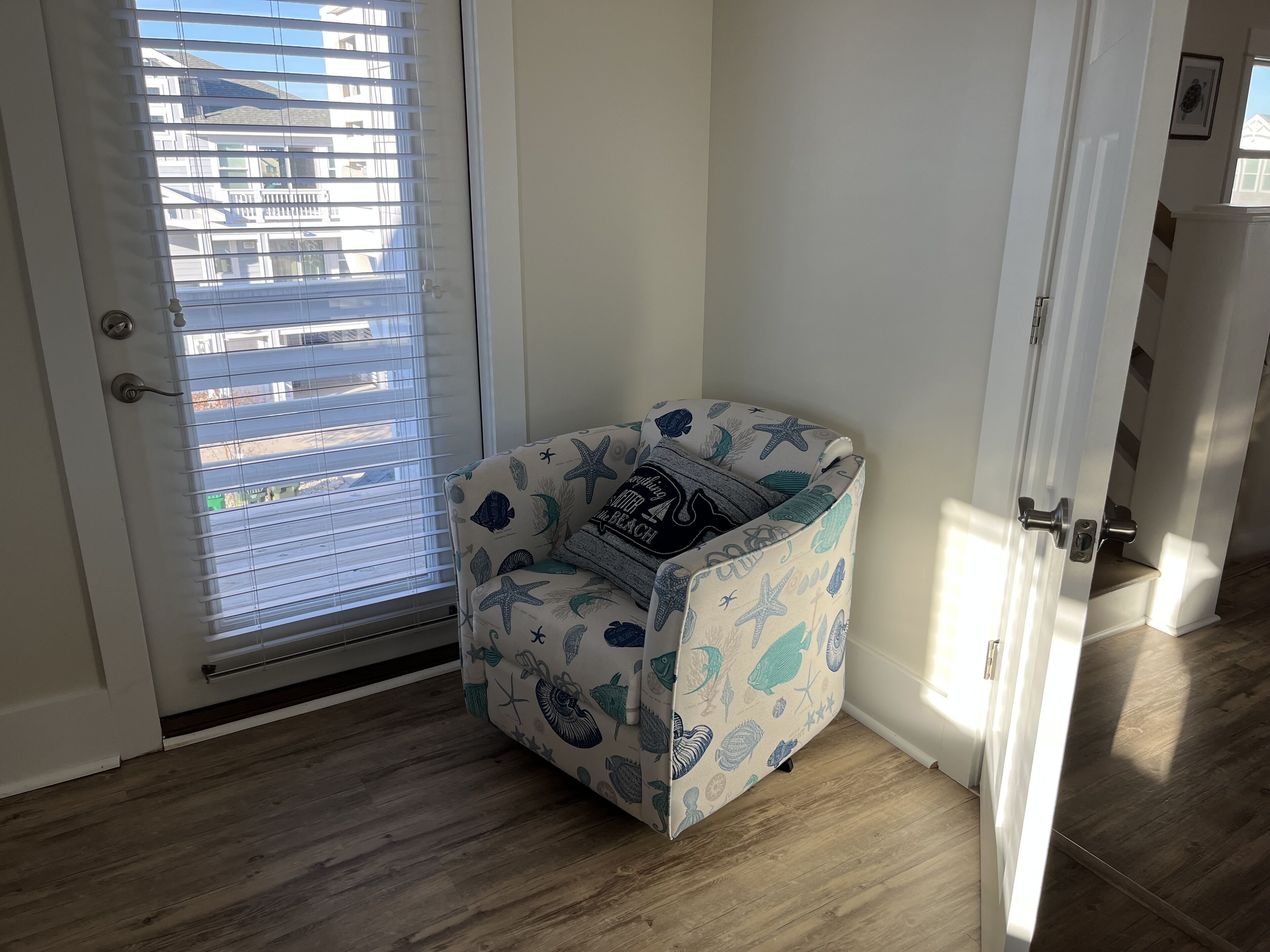 A corner room with a small chair, a door, and a window with blinds.
