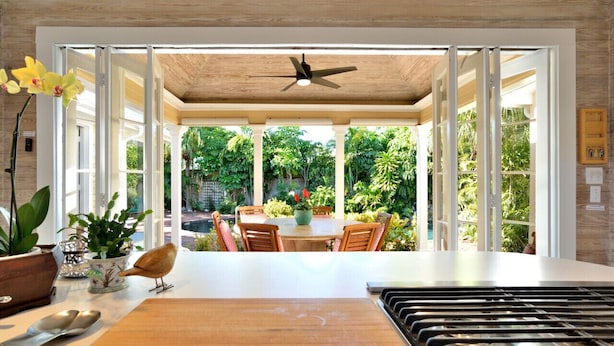 Una cocina moderna con una isla central, un ventilador de techo y vistas a un jardín exuberante a través de puertas abiertas.