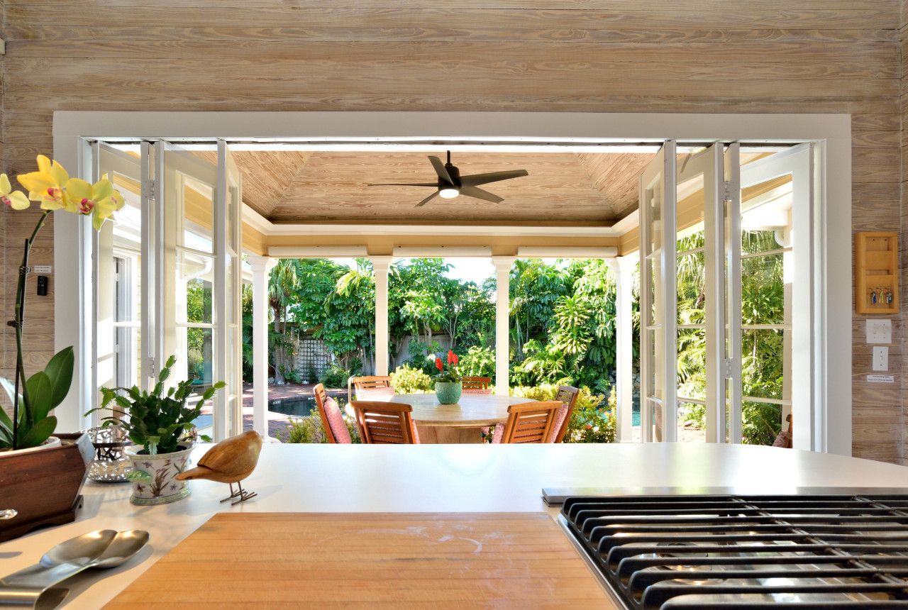 A modern kitchen with a central island, a ceiling fan, and a view of a lush garden through open doors.