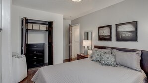 Een slaapkamer met een bed, een dressoir, een kast en twee foto’s in lijsten aan de muur.