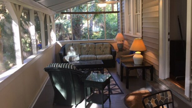 A covered porch with a sofa, chairs, and a table, featuring large windows and a lamp. - Privacy and Seclusion - Marsh View  150 Yards from Front Beach (Folly Beach)