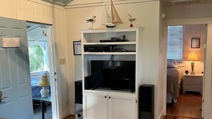 A living room with a ceiling fan, a TV on a white entertainment unit, a patterned rug, and wooden flooring. - Privacy and Seclusion - Marsh View  150 Yards from Front Beach (Folly Beach)