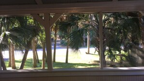 A view through a window with a wooden frame, palm trees, and a road in the background. - Privacy and Seclusion - Marsh View  150 Yards from Front Beach (Folly Beach)