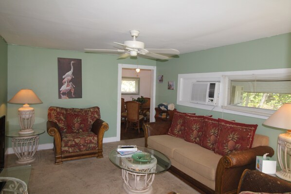 A living room with a ceiling fan, two sofas, a coffee table, and a dining area in the background.