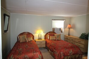 A bedroom with two single beds, a nightstand with a lamp, a dresser, and a window with blinds.